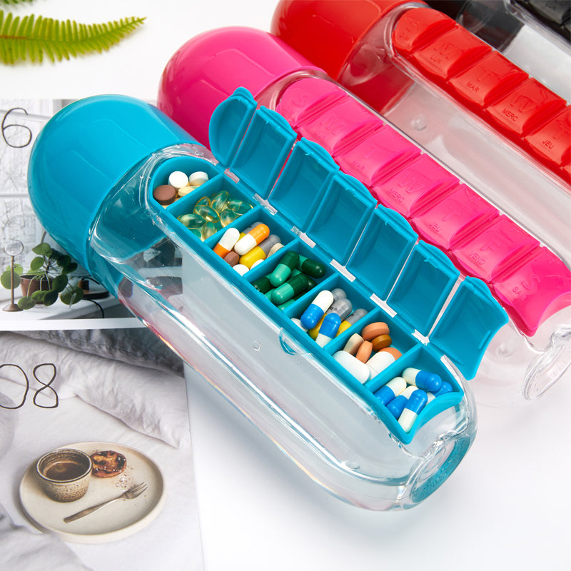 Blue pillbox water bottle open showing daily vitamins and pills sorted by day, styled on a nightstand